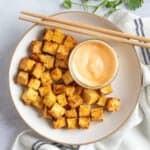 Air fryer tofu cubes with a dipping sauce and chopsticks.