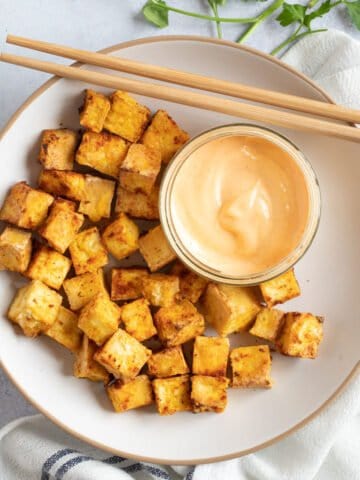 Air fryer tofu cubes with a dipping sauce and chopsticks.