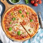 Meat feast pizza on a wooden cutting board.