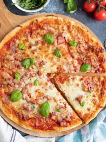 Meat feast pizza on a wooden cutting board.