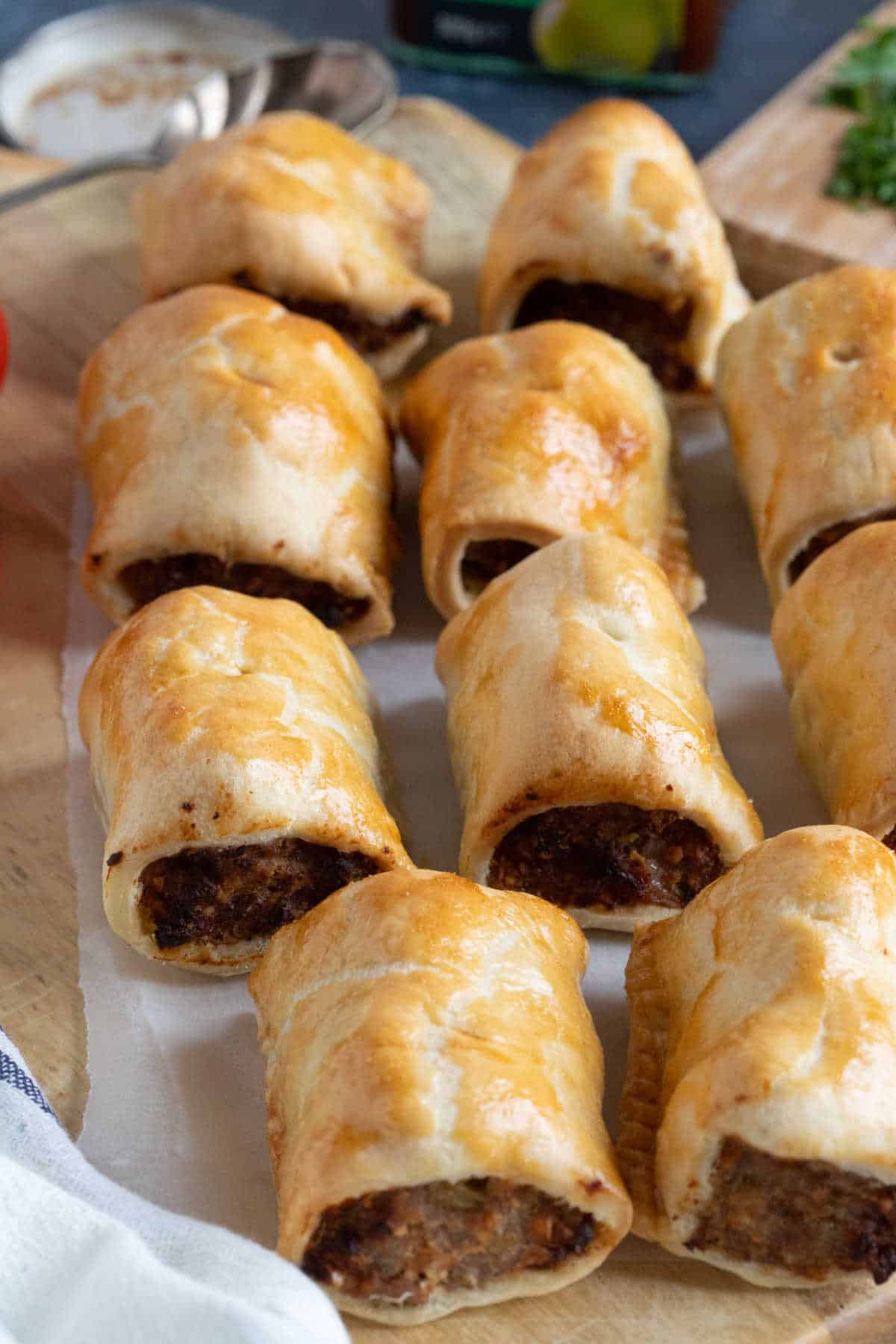 Shortcrust pastry sausage rolls on a wooden board.