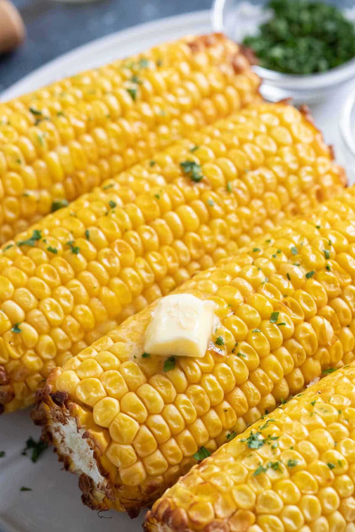 Corn on the cob on a white plate brushed with melted butter.