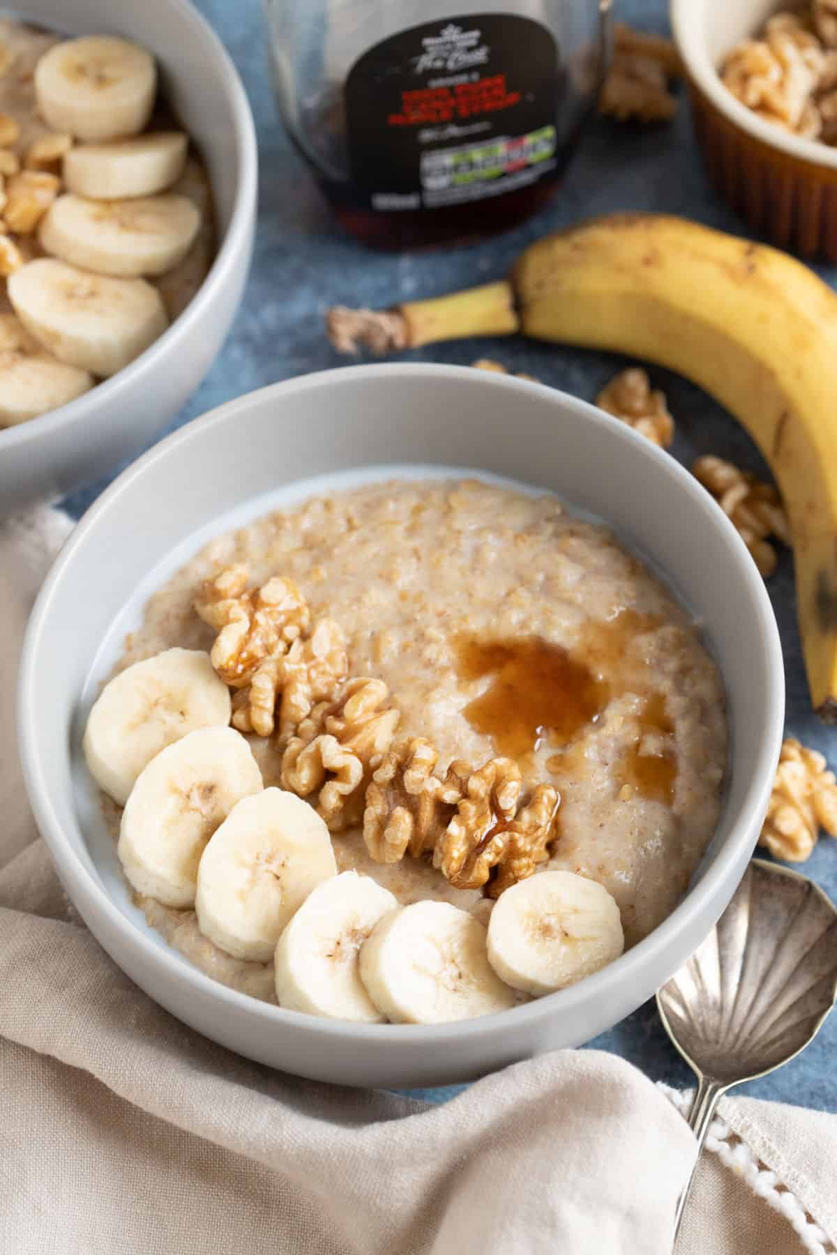 A bowl of banana porridge topped with sliced banana and walnuts.