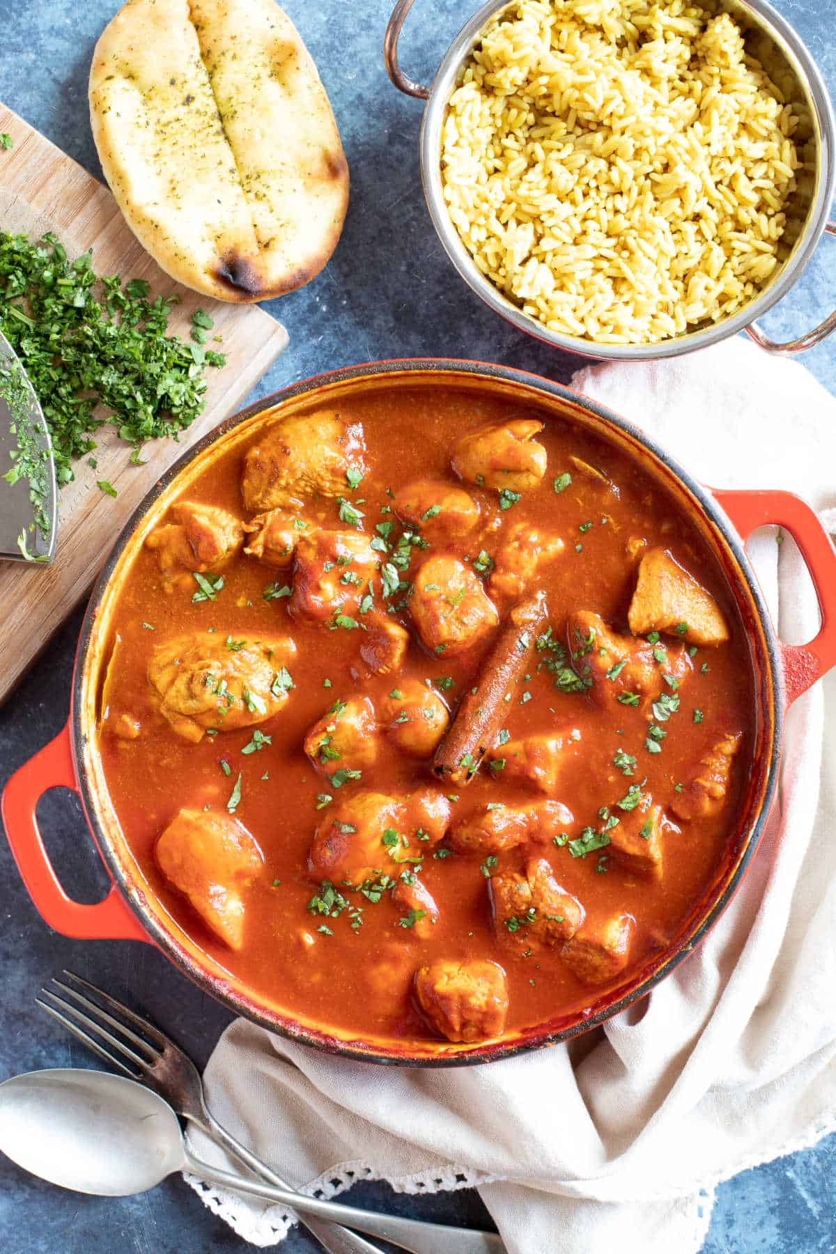 Chicken rogan josh curry in a red pan with a bowl of pilau rice.