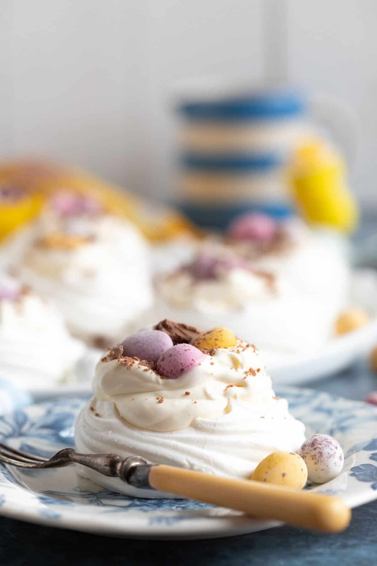 Easter meringue nest on a blue plate topped with Cadbury mini eggs.