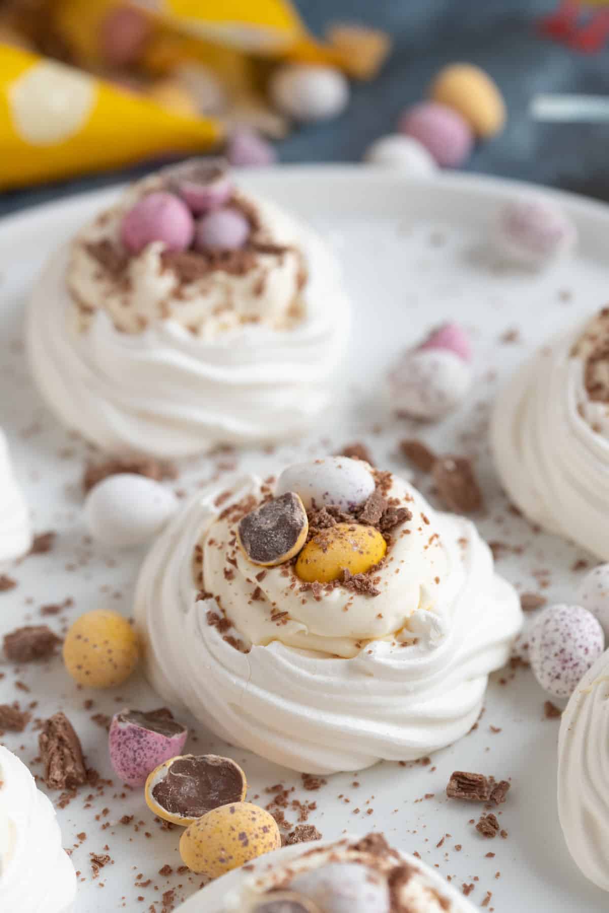 Meringue nests filled with cream and mini eggs on a white plate.