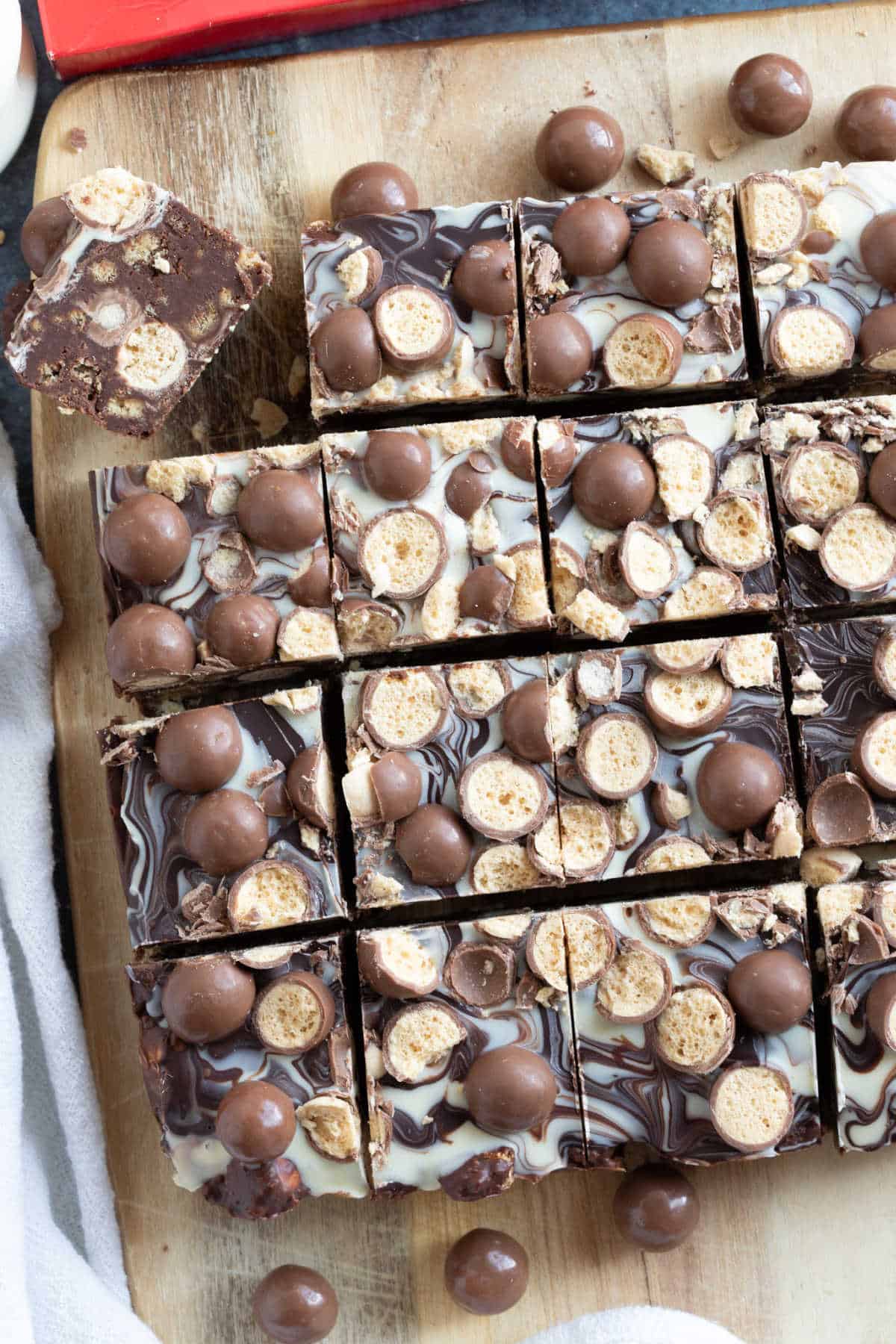 Overhead shot of Malteser tiffin on a wooden board, cut into bars.