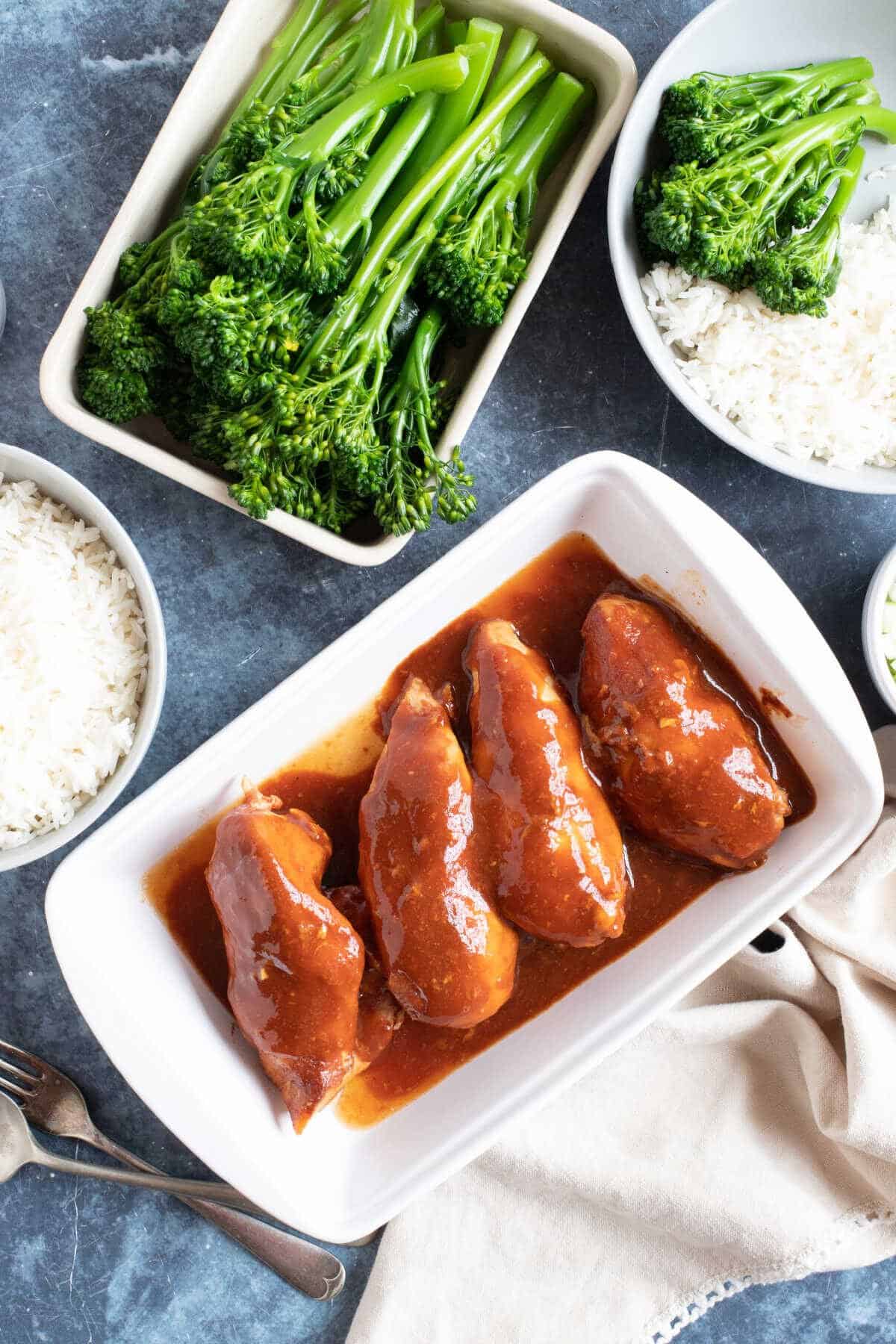 SLow cooker diet coke chicken in a white serving dish with rice and broccoli sides.