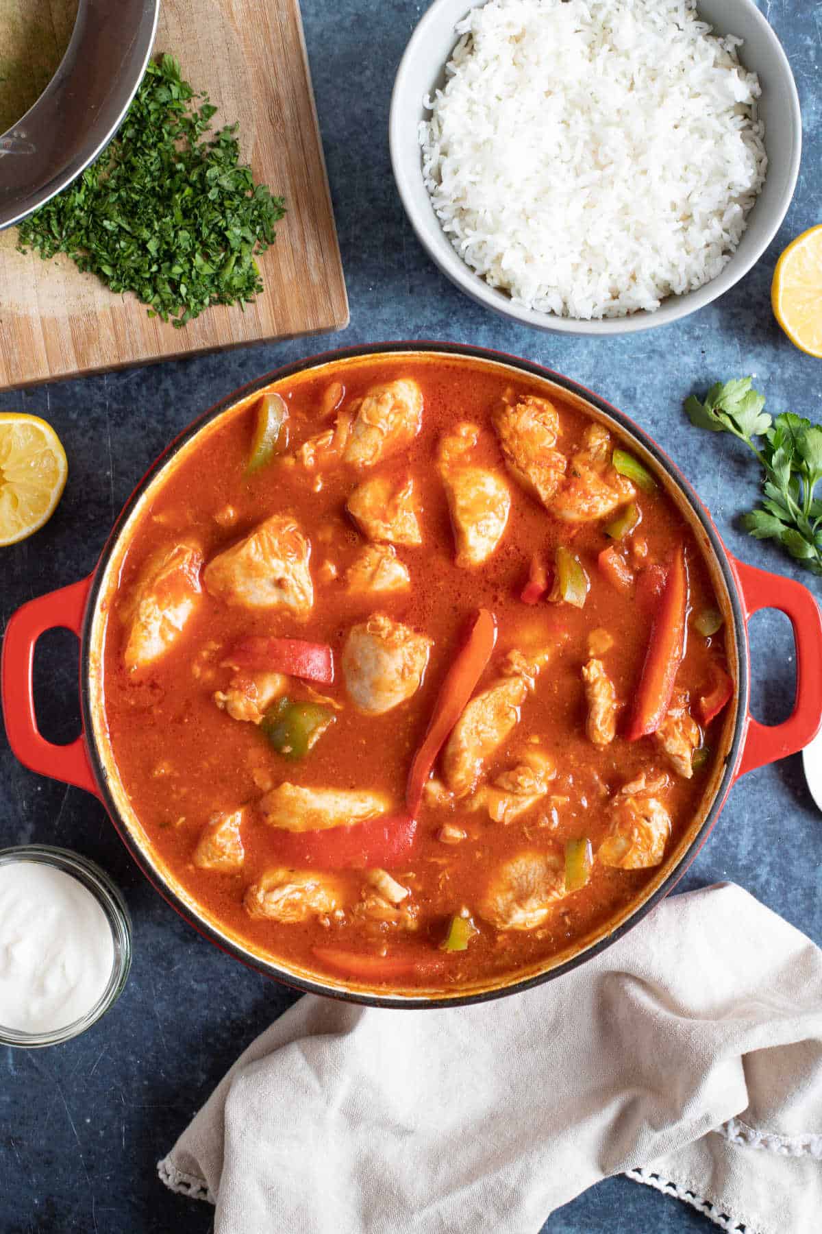 Chicken goulash in a red pan with rice and parsley.