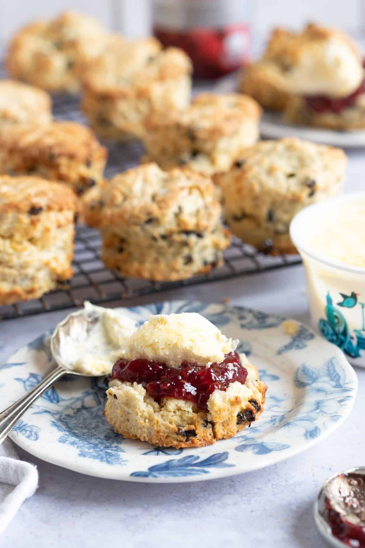 Fruit scone on a blue plate with jam and cream.