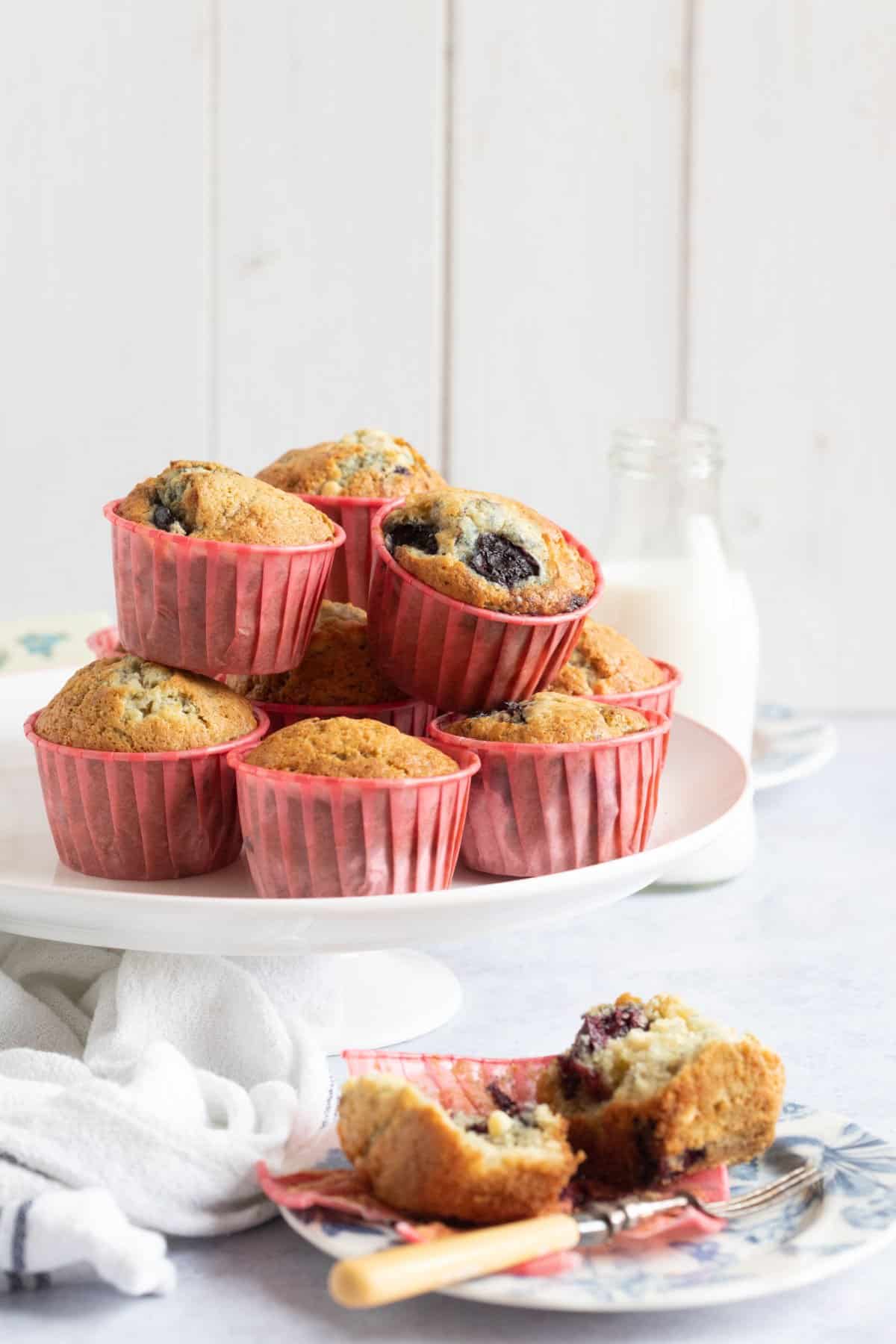 Cherry muffins on a cake stand with one muffin on a blue plate in front of the cake stand.