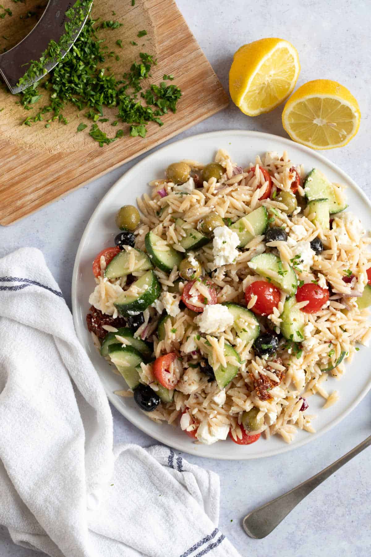 Greek pasta salad with lemon wedges.