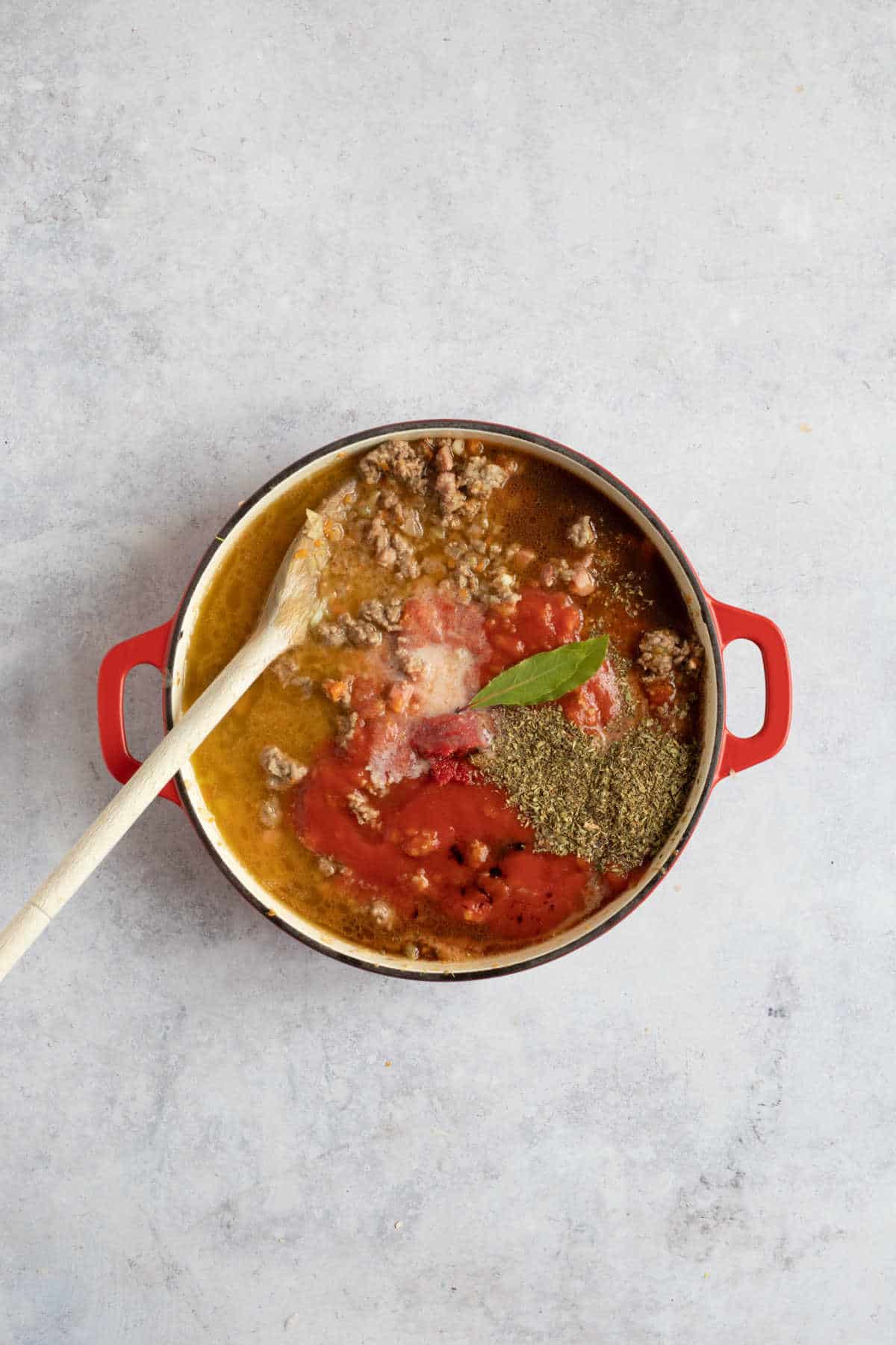 Adding the tomatoes, stock and herbs to the lamb bolognese.