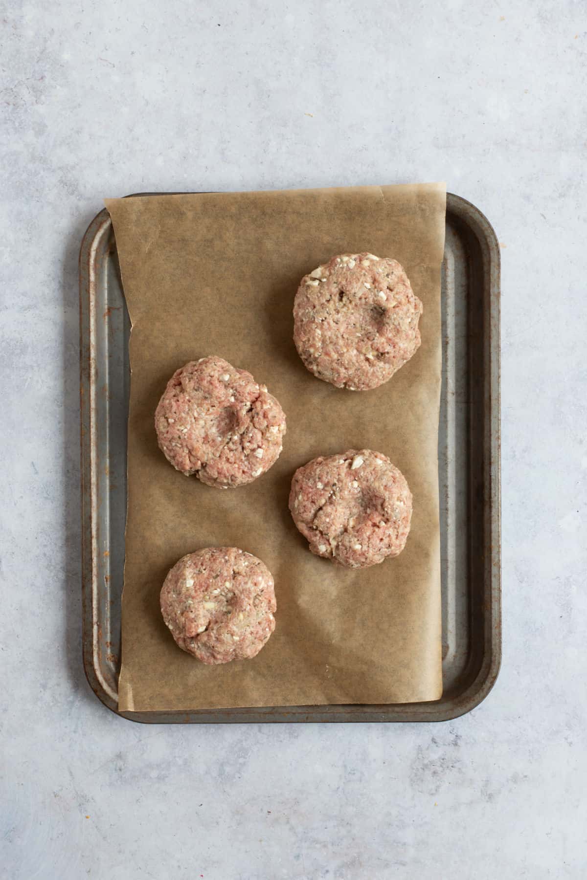 4 lamb and feta burgers on a baking tray.