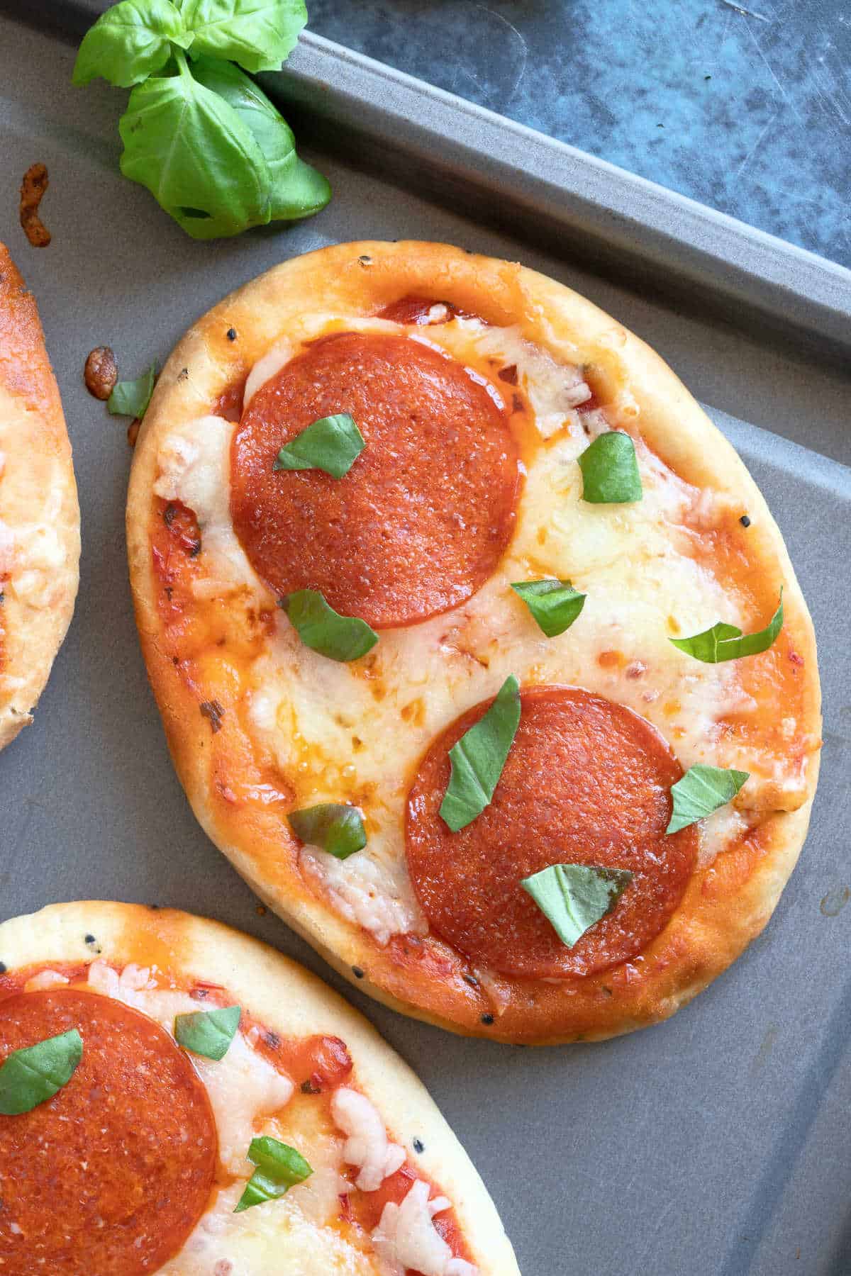 Mini naan bread pizzas topped with pepperoni on a baking sheet.