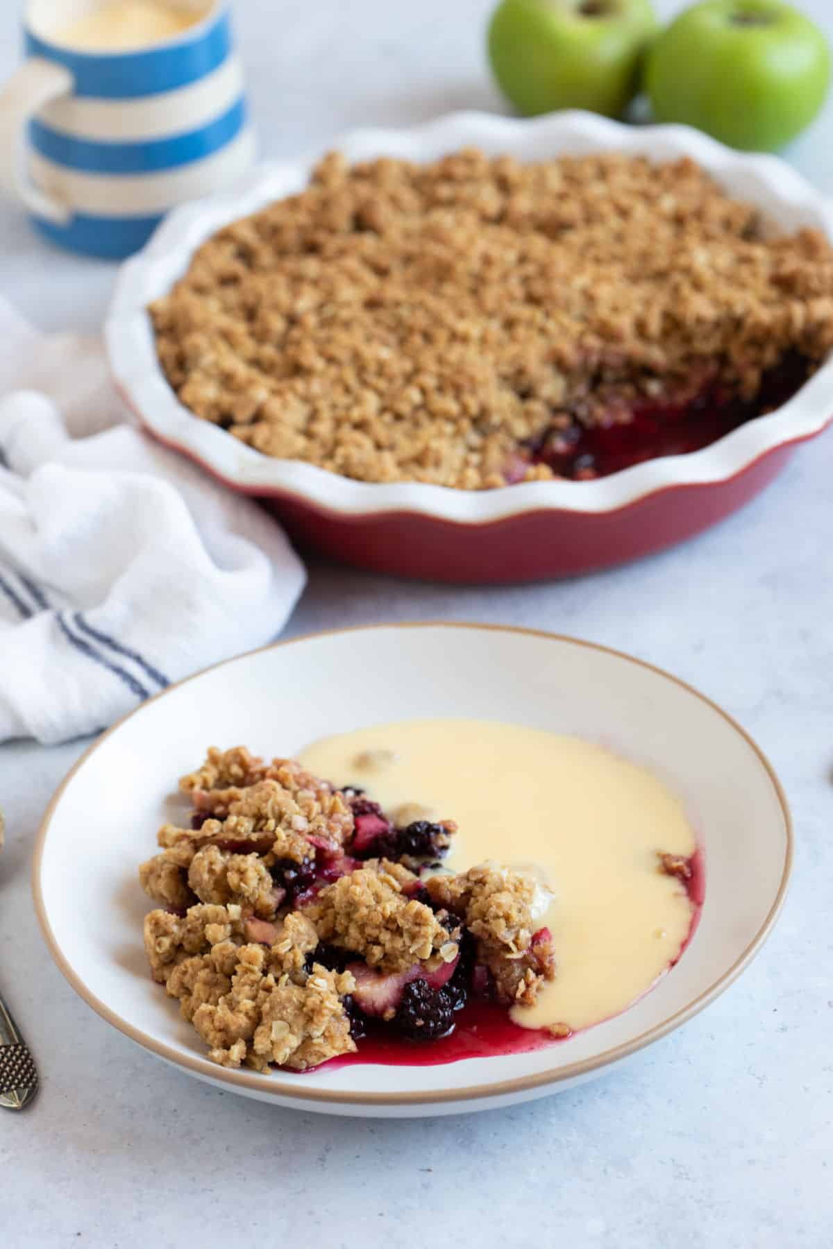 A bowl of blackberry and apple crumble with custard.