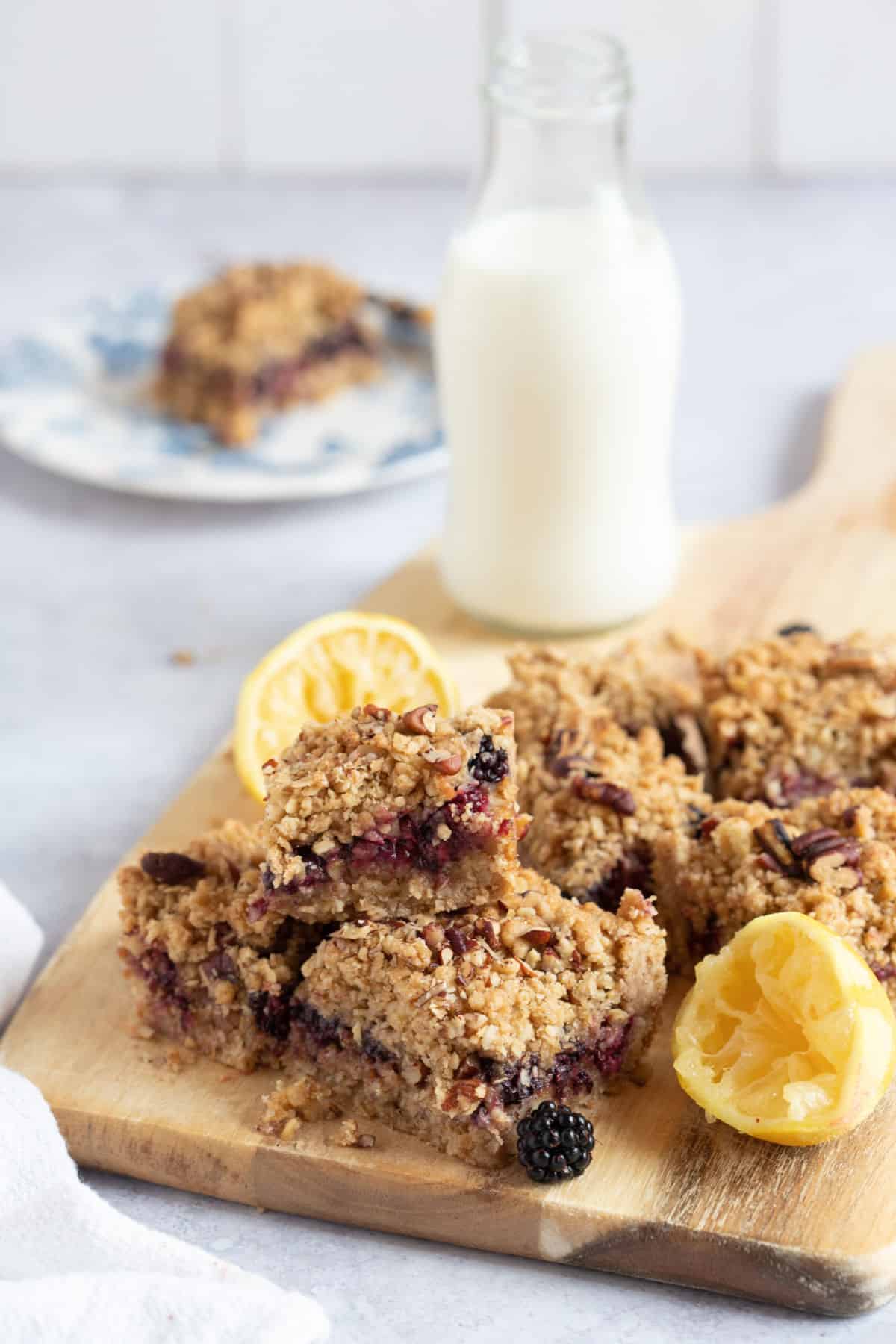 Blackberry crumble bars on a chopping board with a glass of milk.