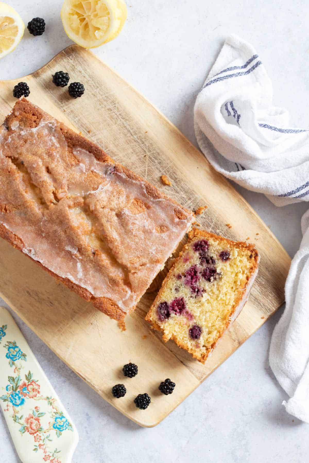 Blackberry loaf cake with a lemon drizzle sugar topping on a wooden board.