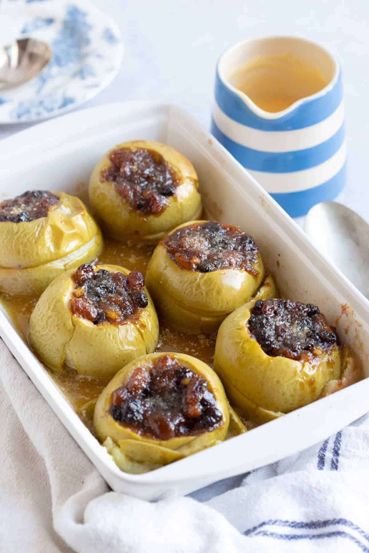Baked apples in a white pie dish with a jug of custard.