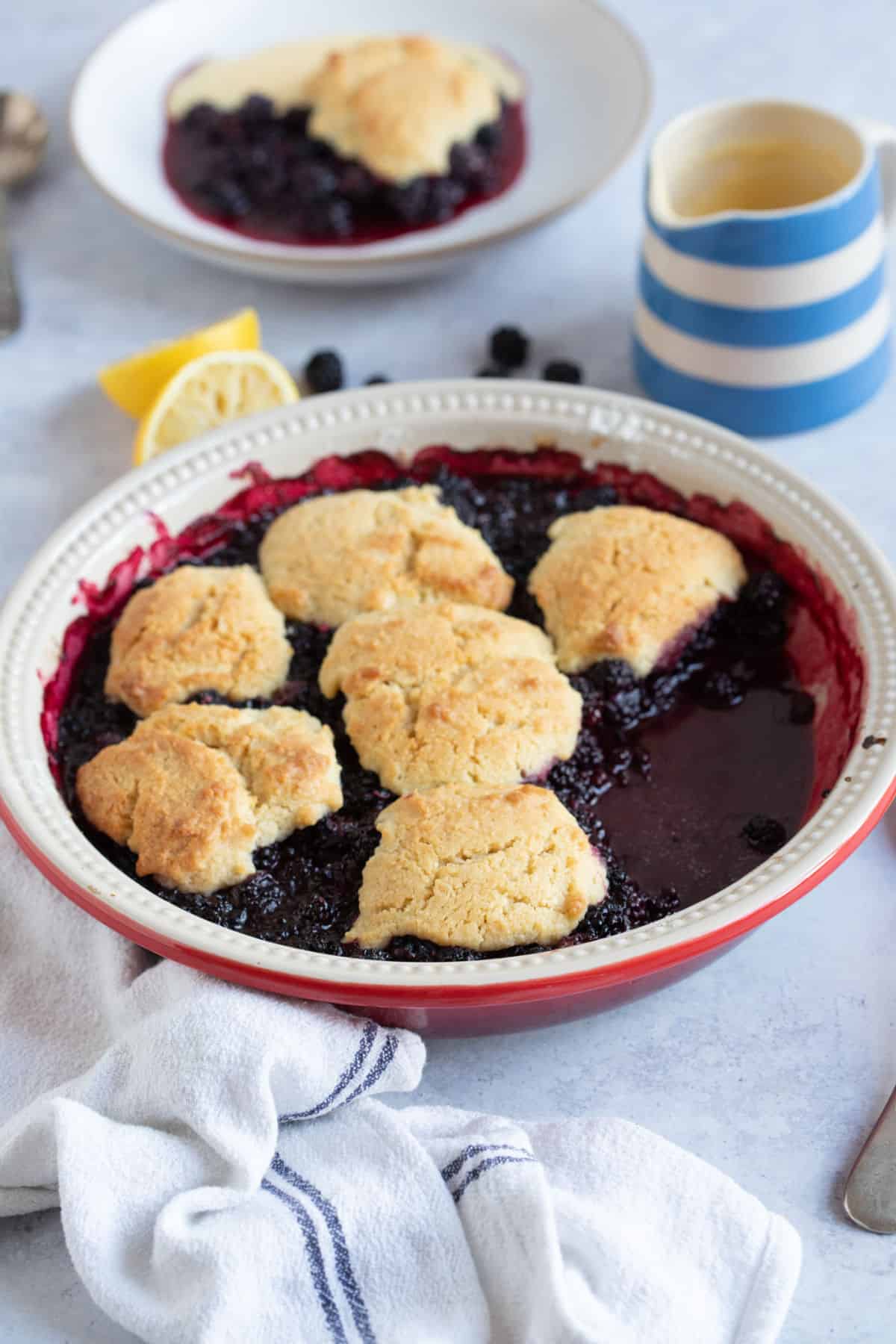 Blackberry cobbler in a pie dish with a jug of custard.
