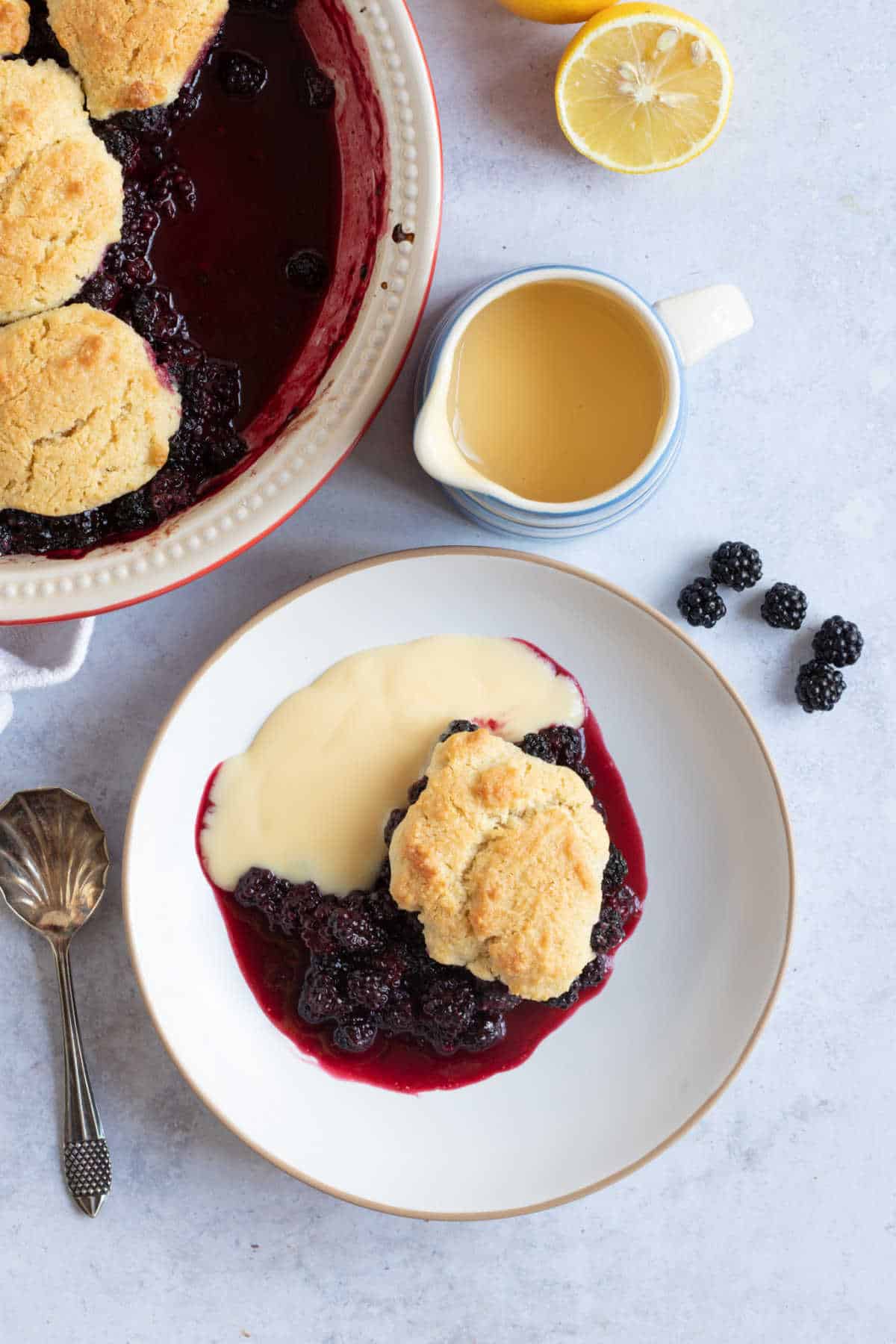 Blackberry cobbler in a baking dish with a jug of custard.