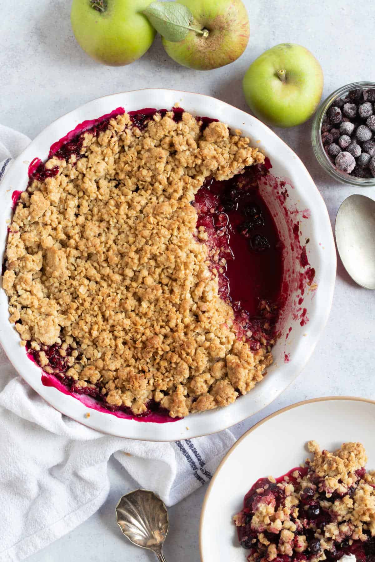 Blackcurrant and apple crumble in a pie dish with a bowl of crumble on the side.