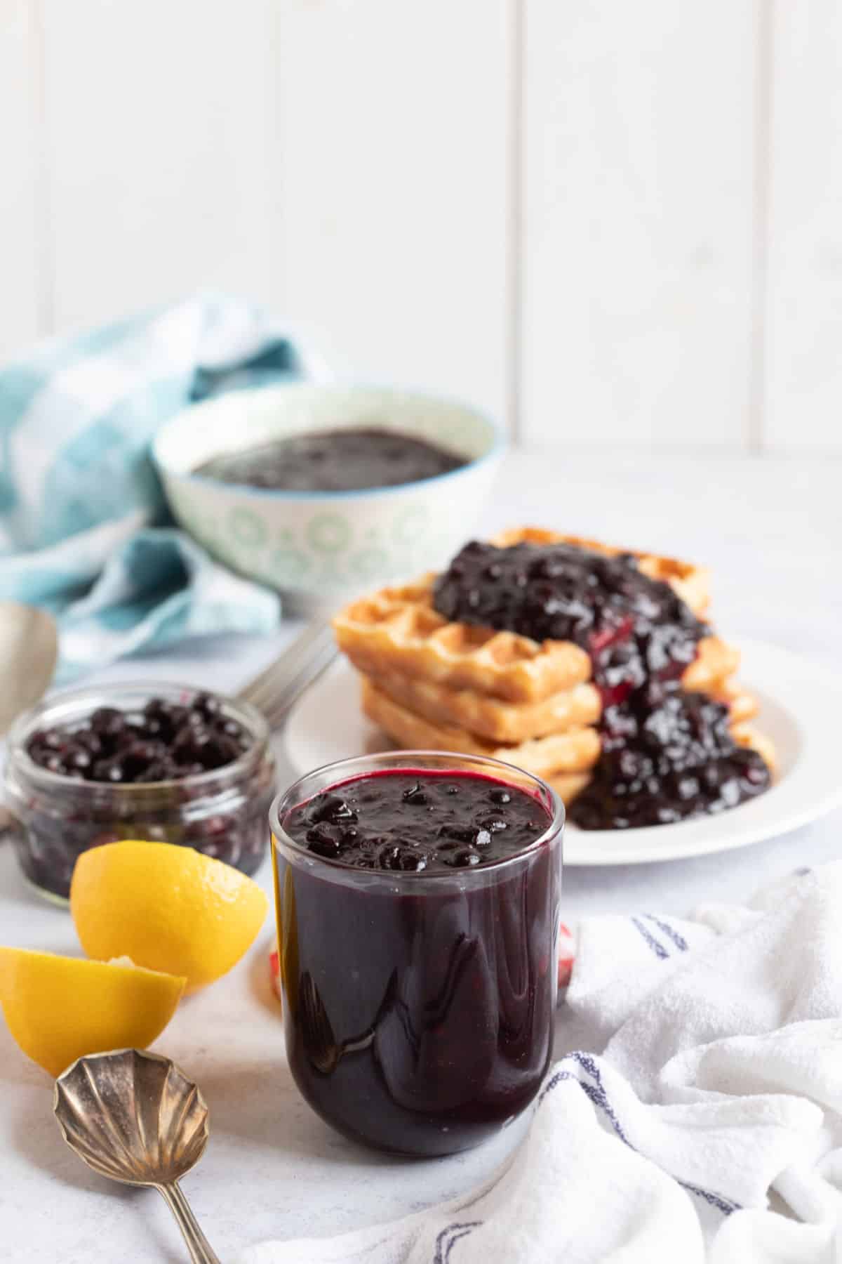 A jar of fruit compote with waffles behind on a plate.