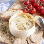 A wheel of air fried camembert on a wooden board with slices of baguette.