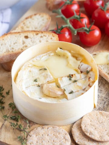 A wheel of air fried camembert on a wooden board with slices of baguette.
