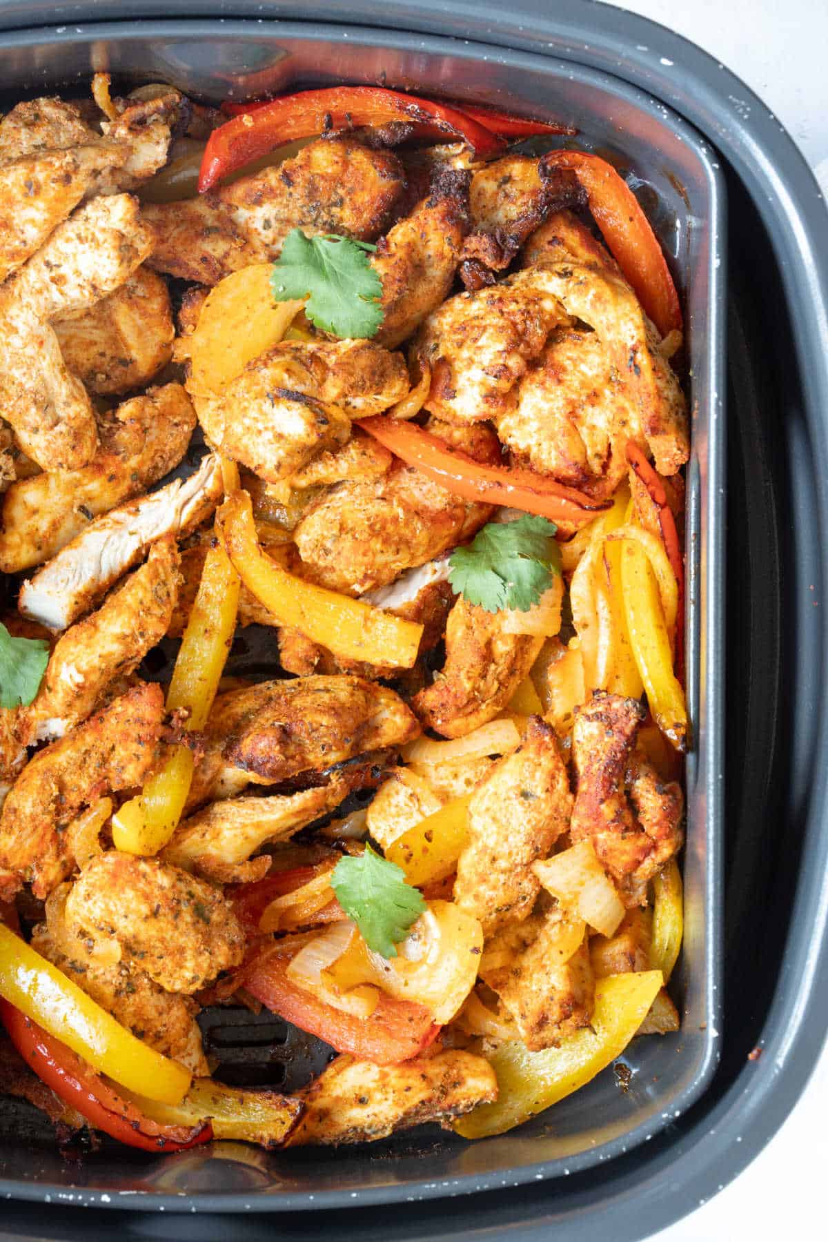 Chicken fajitas in an air fryer basket.