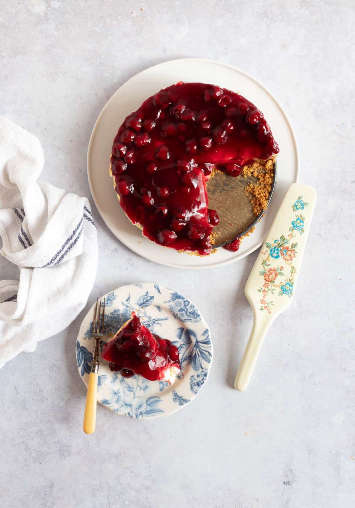 A cherry cheesecake on a serving plate, with a slice taken out.