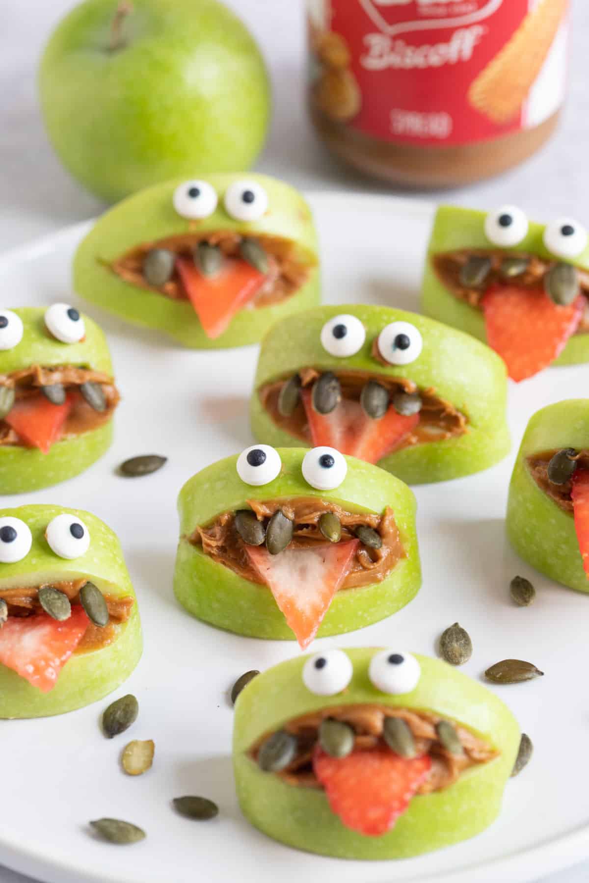 Halloween green apple monsters on a plate with pumpkin seeds.