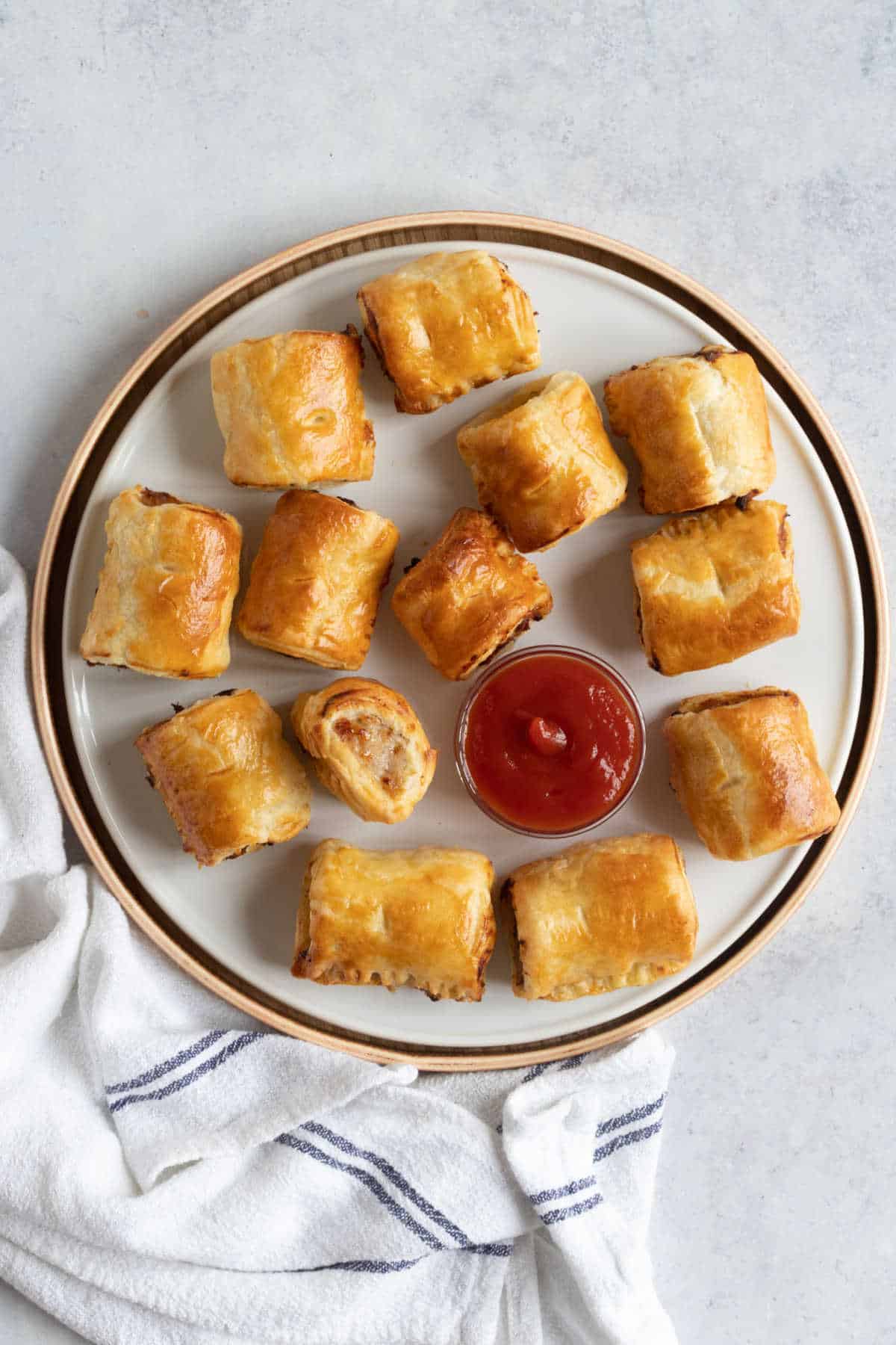 A plate of sausage rolls with a pot of ketchup.