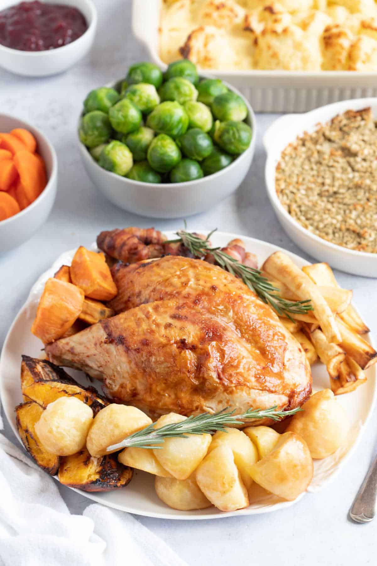 Air fryer turkey crown on a platter with roast potatoes and parnsips.