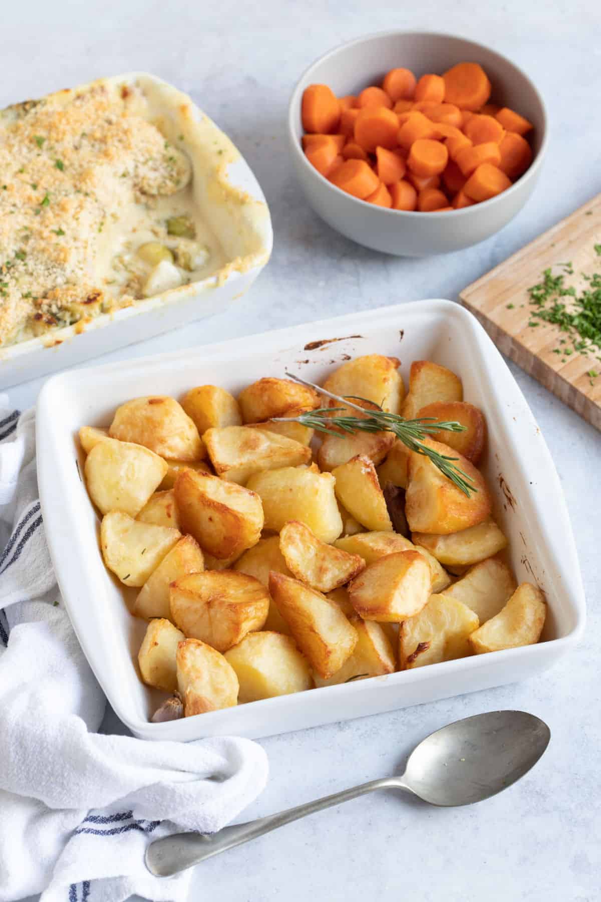 Duck fat roast potatoes in a white serving dish with a sprog of rosemary.