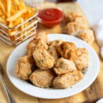 Air fried chicken nuggets on a white plate with fries and ketchup.