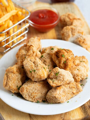 Air fried chicken nuggets on a white plate with fries and ketchup.