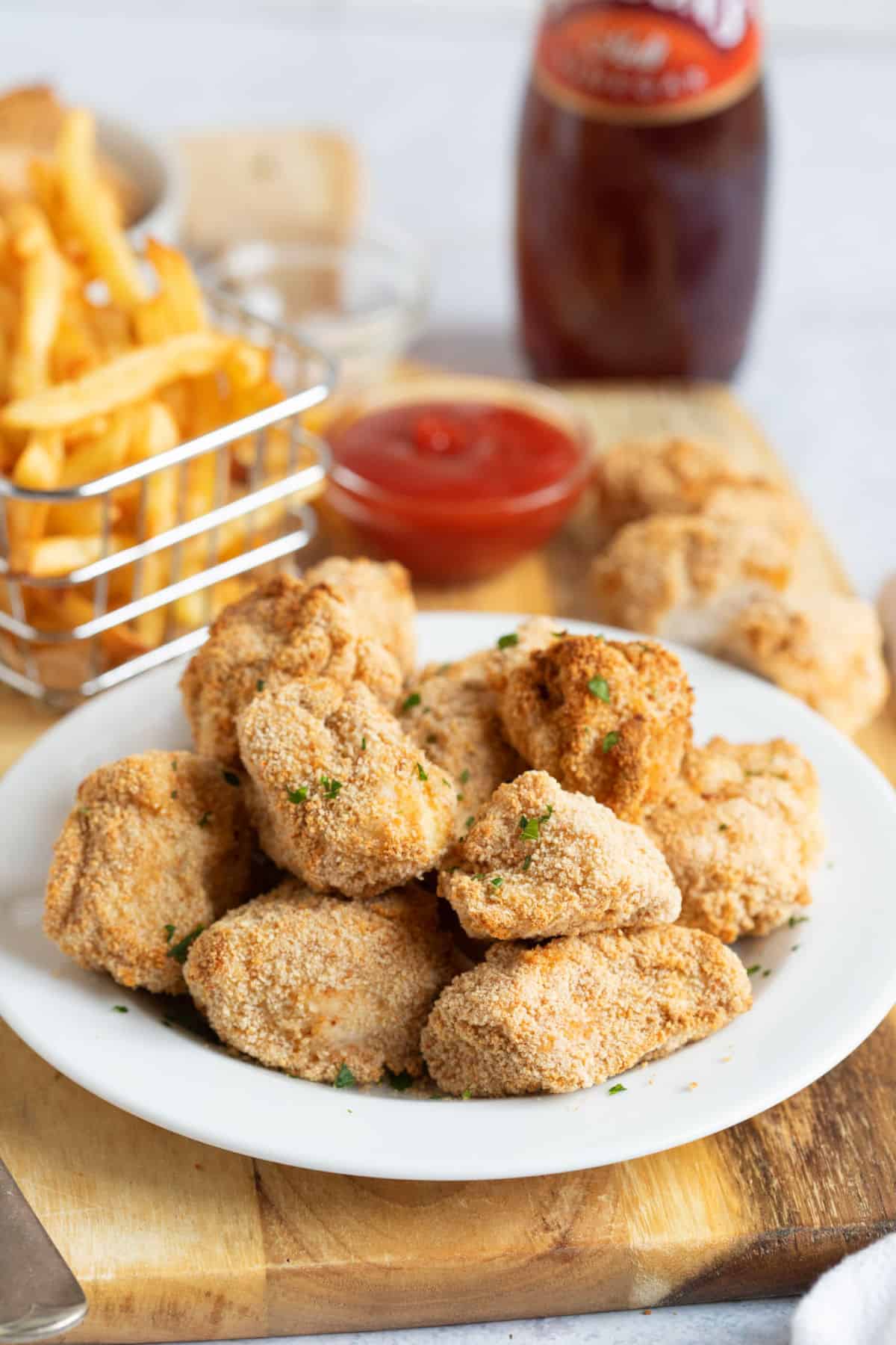 Air fryer chicken nuggets on a white plate with fries and ketchup.