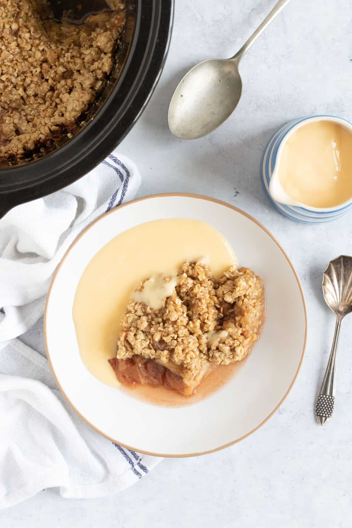 Crock pot apple crumble in a bowl with custard.