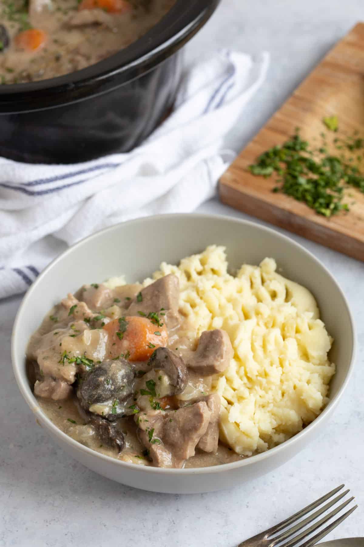 Pork and apple casserole in a bowl with mashed potato.