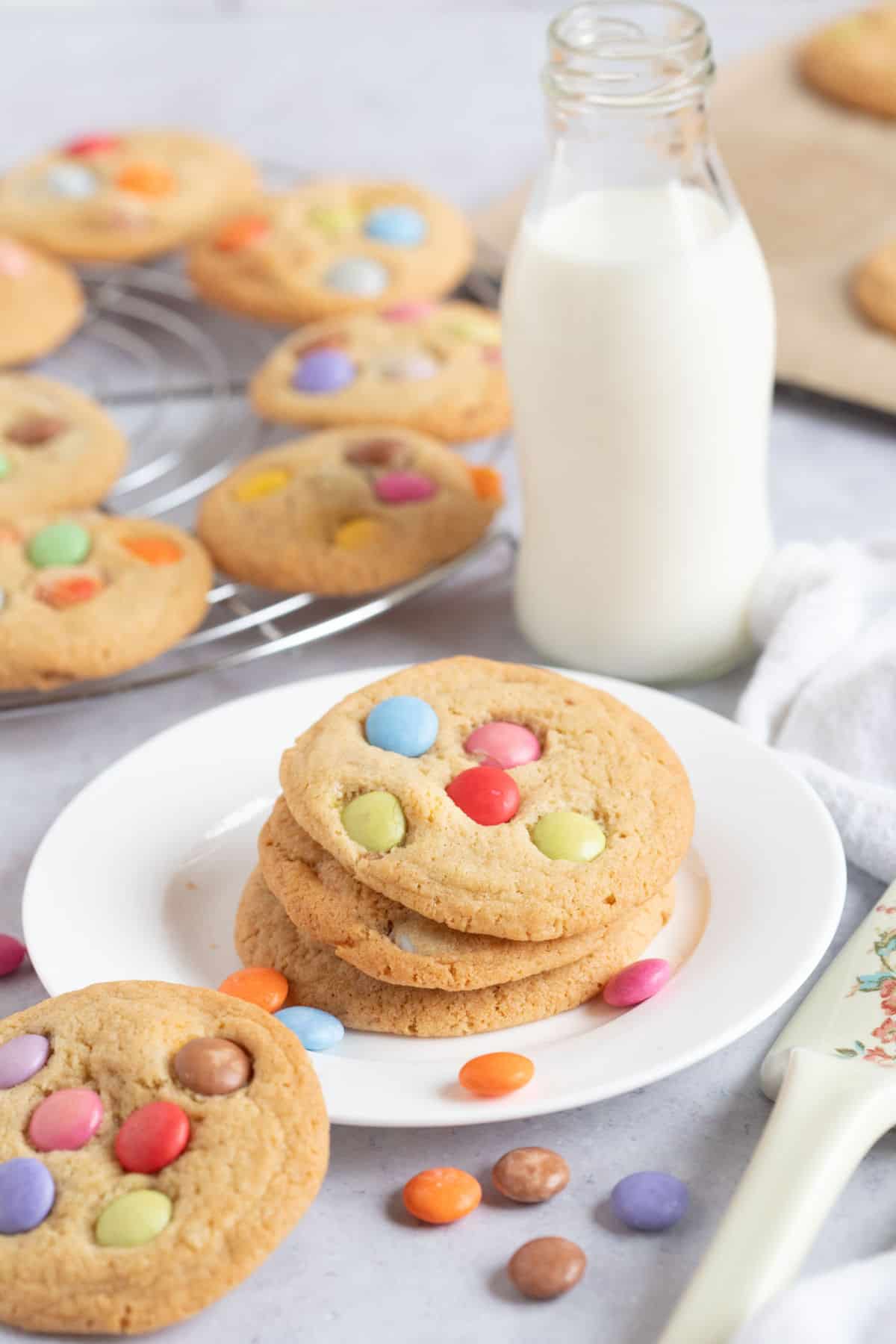 A stack of smarties cookies on a plate with a bottle of milk.