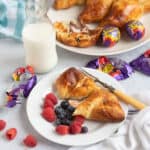 Air fryer creme egg croissant on a plate with raspberries and blueberries and a glass of milk in the background.