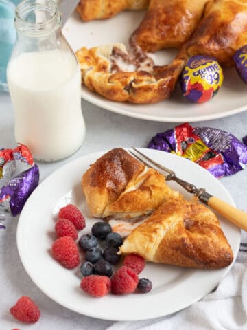 Air fryer creme egg croissant on a plate with raspberries and blueberries and a glass of milk in the background.