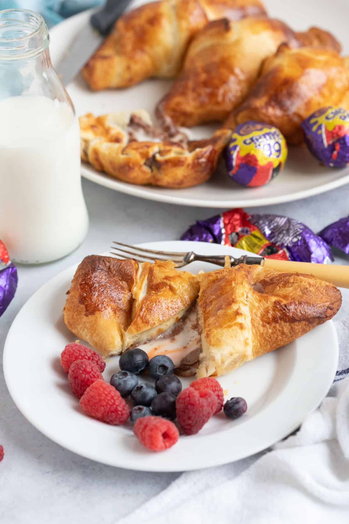 A creme egg croissant pulled in half with the melted chocolate and fondant oozing out onto the white plate.