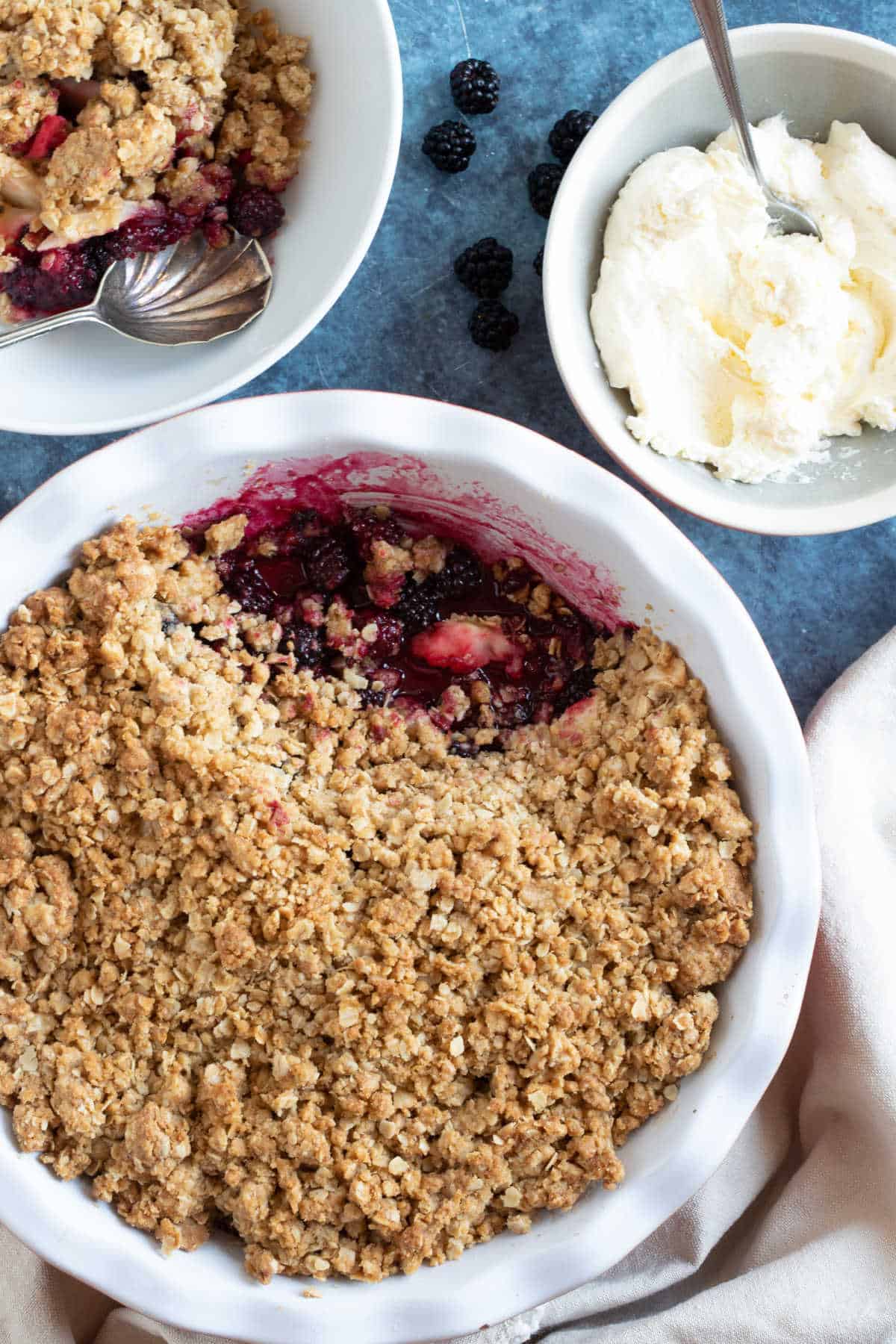 Blackberry crumble in a large baking dish with a bowl of whipped cream on the side.