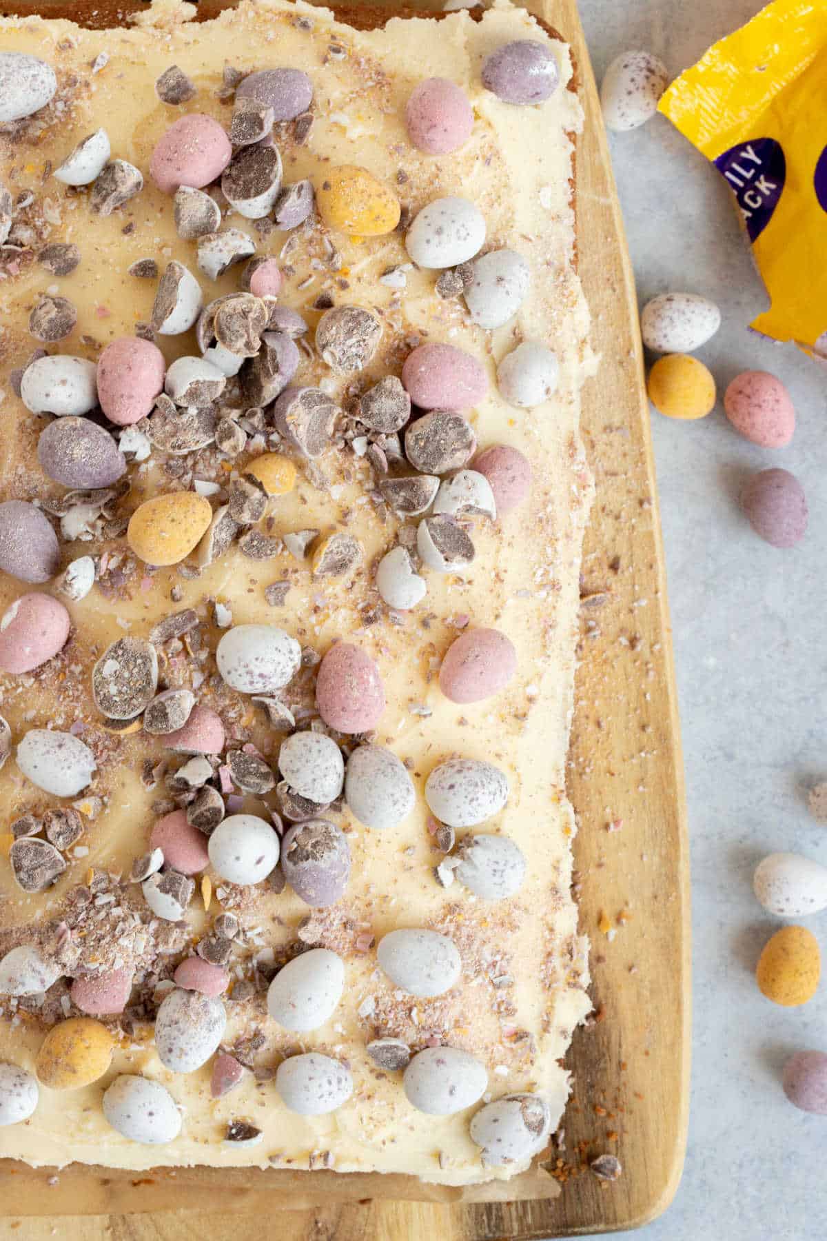 Cadbury mini egg traybake cake on a wooden cake board.