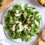 Rocket salad with Parmesan shavings on a white plate.