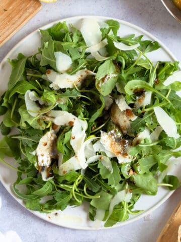 Rocket salad with Parmesan shavings on a white plate.