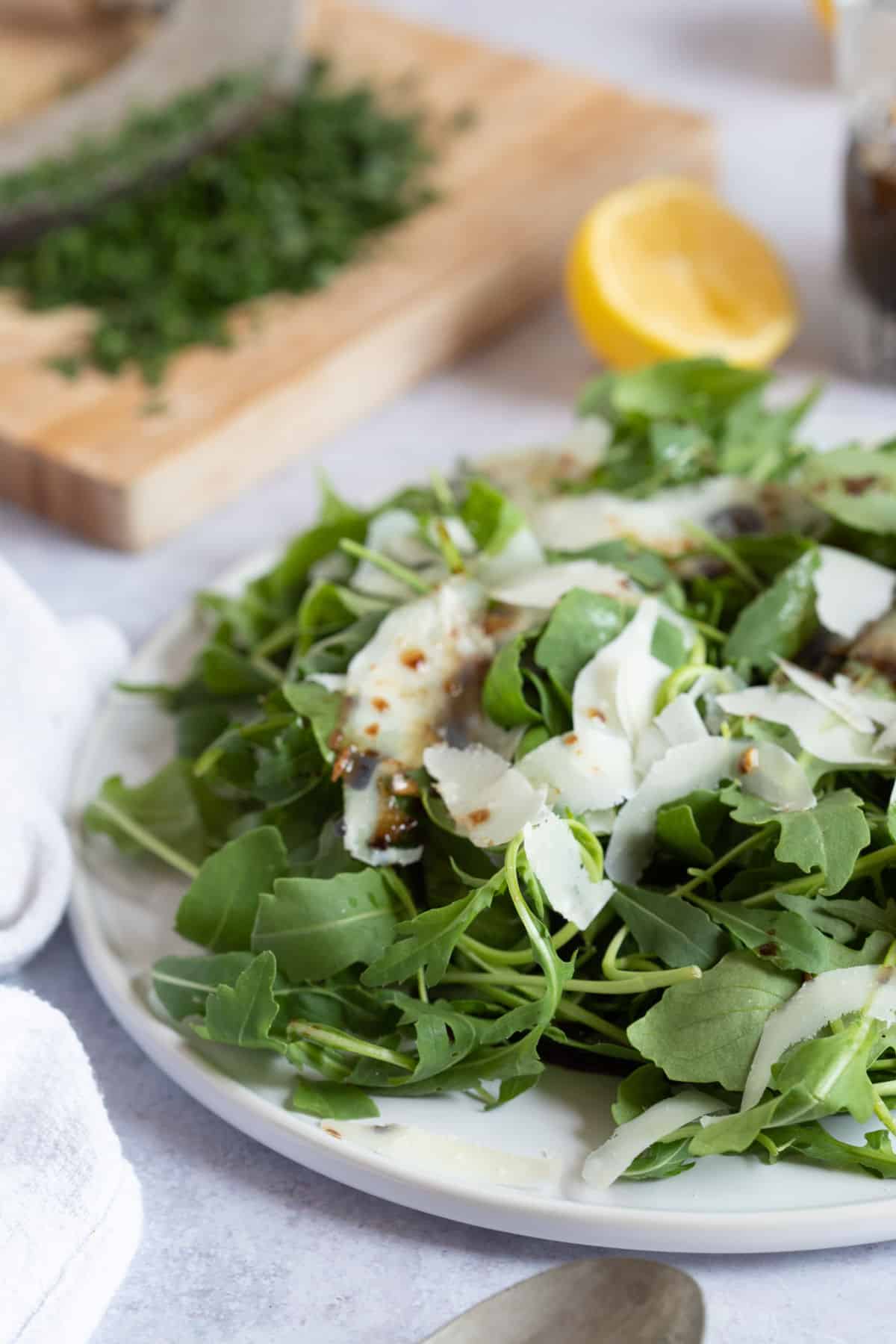 Green salad with Parmesan shavings on a white plate.