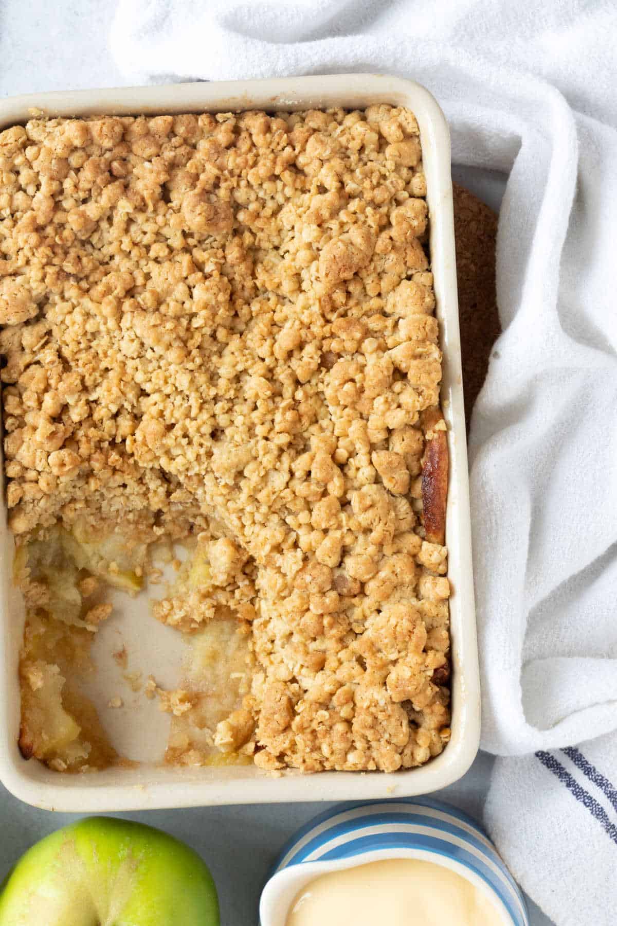 Apple crumble in a rectangular baking dish with a jug of custard.